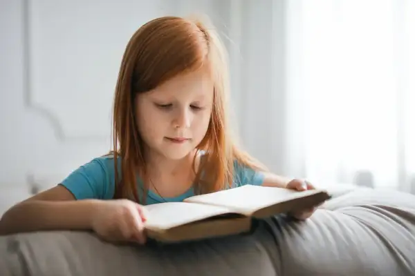 Niña pelirroja concentrada leyendo un libro. Su velocidad lectora por edades es notable para su corta edad.