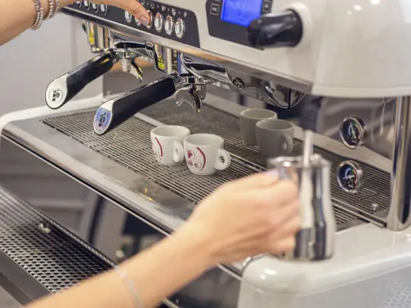 Mano che prepara un caffè con la bar macchina caffè. Due tazzine bianche attendono il loro turno.