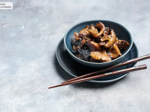 Deliciosas setas shiitake salteadas en un cuenco azul, listas para ser disfrutadas con palillos.