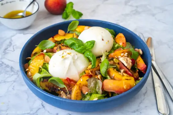 Pfirsich-Burrata-Salat mit Nüssen und Basilikum in blauer Schüssel.