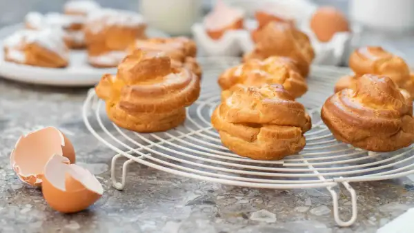 Färska petit choux på ett galler, med äggskal i förgrunden. Perfekt för en fika!