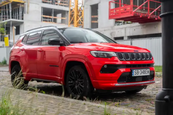Czerwony Jeep Compass 2025 z czarnymi felgami na tle budowy.