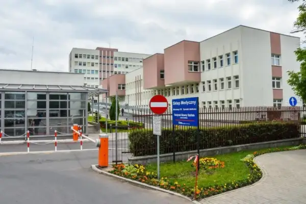 Nowoczesny budynek szpitala z bramkami wjazdowymi i znakami informacyjnymi.