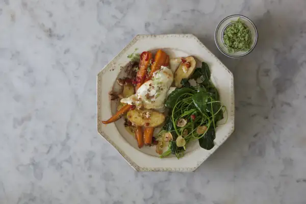 Ugnsrostade rotfrukter med fetaost, serverade med gröna blad och en grön topping.