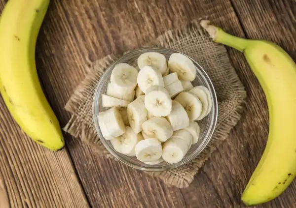 Dwa banany, jeden w całości, drugi pokrojony w plasterki w szklanej miseczce. Zastanawiasz się, ile węglowodanów ma banan?