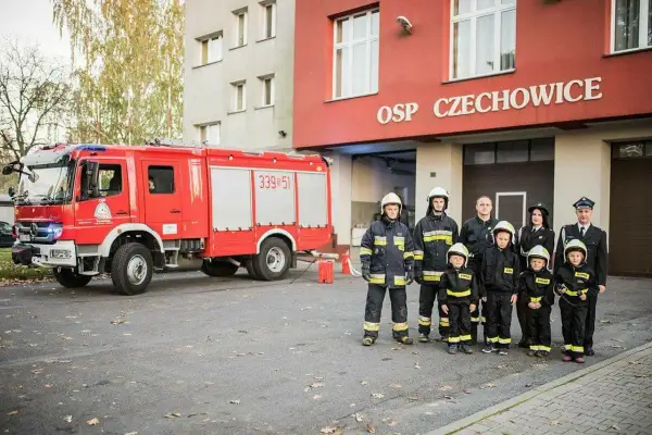 Strażacy OSP Czechowice z wozem strażackim i dziećmi w strojach strażackich.