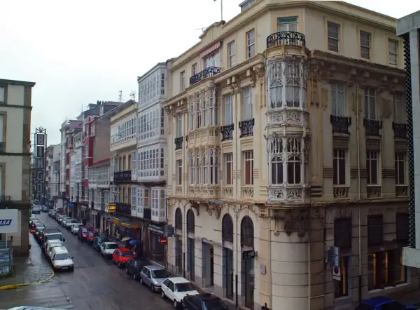 Edificios con balcones acristalados y una torre ornamental en una calle de Ferrol. Merece la pena visitar Ferrol por su arquitectura única.