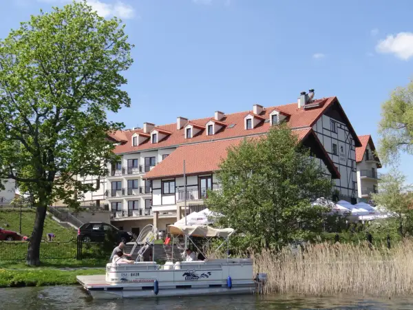 Hotel Anek Mrągowo nad jeziorem, z łodzią przy pomoście i zielenią.