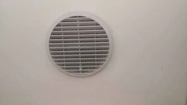 Foro ventilazione cucina entra freddo. La griglia bianca circolare è montata su una parete chiara.