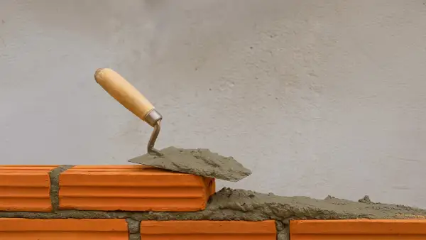 Cazzuola con malta a base di calce pronta per posare un mattone su una parete in costruzione.