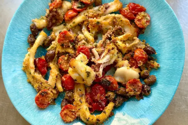Deliziosi calamari gratinati al forno, croccanti e saporiti, con pomodorini e olive, serviti su un piatto blu.