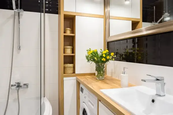 Petite salle de bain avec baignoire, lavabo, machine à laver et étagères en bois. Un bouquet de fleurs jaunes décore le plan de travail.