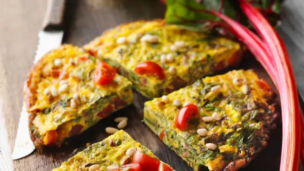 Tortilla de acelgas con tomates cherry y piñones, cortada en porciones sobre una tabla de madera.