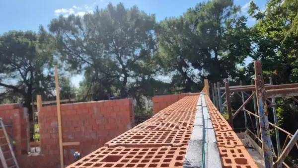 Costruzione di una muratura portante in laterizio, con mattoni forati rossi e blocchi in cemento.
