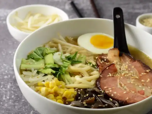 Jak zrobić ramen? Miska pełna aromatycznego bulionu z makaronem, plastrem boczku, jajkiem na pół, pak choi, kukurydzą i grzybami mun.