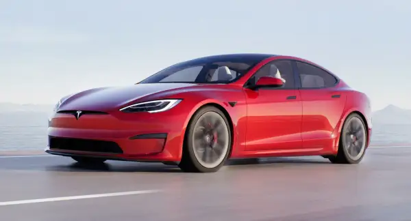 Czerwony Tesla Plaid pędzi po drodze, z widokiem na morze i góry w tle.