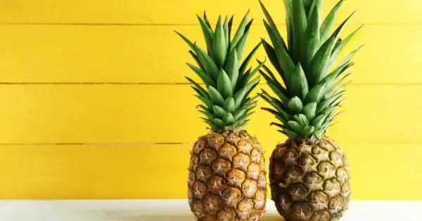 Dwa soczyste ananasy na tle żółtej deski. Poznaj ich bogactwo witamin i minerałów – ananas wartości odżywcze.