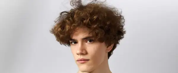 Primer plano de un joven con cabello rizado y castaño sobre fondo blanco.