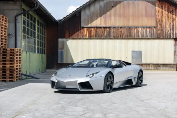 Srebrny, otwarty Lamborghini Reventon stoi przed rustykalnym budynkiem.