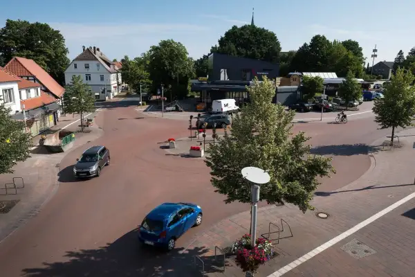 Ein sonniger Tag im **shared space Bohmte**. Autos fahren durch den Kreisverkehr, ein Radfahrer genießt die Fahrt.