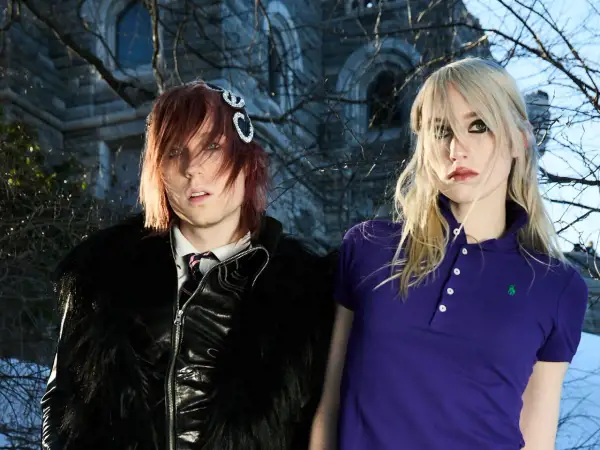 Frost Children setlist: A person with red hair and a black furry jacket stands next to a person with blonde hair in a purple polo shirt.