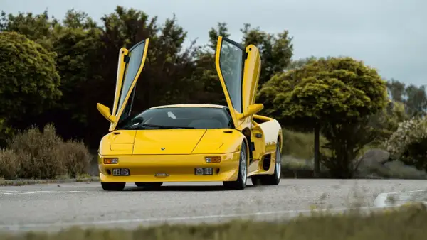 Żółty Lamborghini Diablo z otwartymi drzwiami, zaparkowany na drodze wśród zieleni.