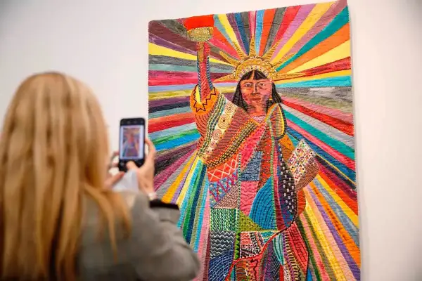 A woman photographs a vibrant quilt depicting the Statue of Liberty, a powerful piece by Asian American artists celebrating diversity.
