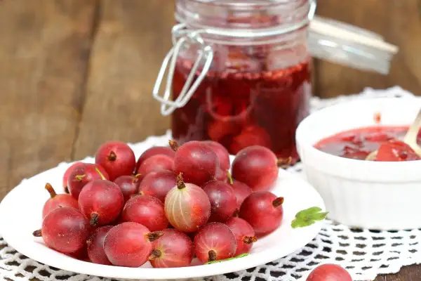 Frische Stachelbeeren auf einem Teller, daneben ein Glas mit Stachelbeermarmelade und eine Schale mit Marmelade. Perfekt, um sie mit Joghurt zu mischen.