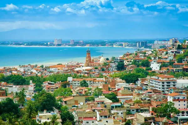 Vista panorámica de una ciudad costera en México, con casas de tejas rojas, una iglesia con cúpula y edificios modernos junto al mar azul. ¡Un sueño para vivir en México!