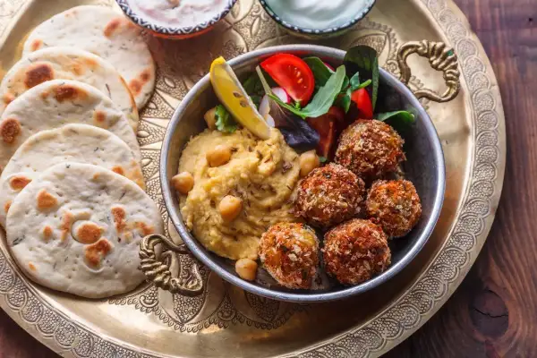Pyszne jedzenie koszerne: hummus, falafel, świeże pieczywo i sałatka na ozdobnej tacy.