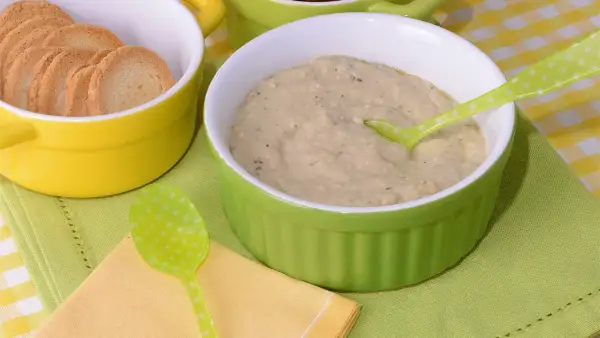 Un cremoso puré de berenjena servido en un cuenco verde, acompañado de galletas tostadas en un cuenco amarillo.