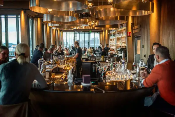 Människor sitter vid en bar med många flaskor och glas. Belysningen är varm och stämningen inbjuder till att läsa **spesso recensioner** om stället.