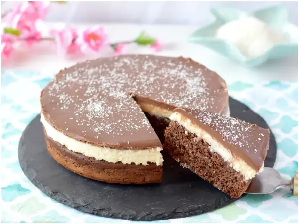 Deliziosa torta cocco e cioccolato con glassa lucida e cocco grattugiato. Una fetta è già servita.