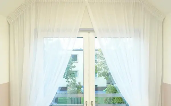 Delikatne, białe firanki upięte na karniszu nad oknem w kuchni, tworzące subtelny efekt.