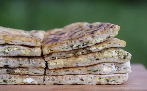 Pile de pains plats au fromage et aux herbes, rappelant l'origine du cheese naan.