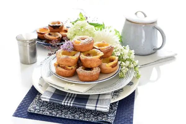 Montón de pastel de nata portugal, espolvoreados con azúcar glas, decorados con flores y servidos en platos de cerámica.