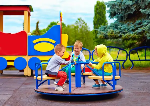 Trzech chłopców bawi się na karuzeli na kolorowym placu zabaw.