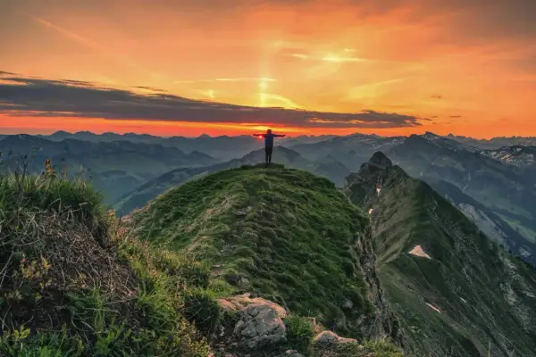 Sonnenuntergang auf der Kanisfluh Wanderung. Ein Wanderer steht mit ausgebreiteten Armen auf dem Gipfel und genießt den atemberaubenden Ausblick.