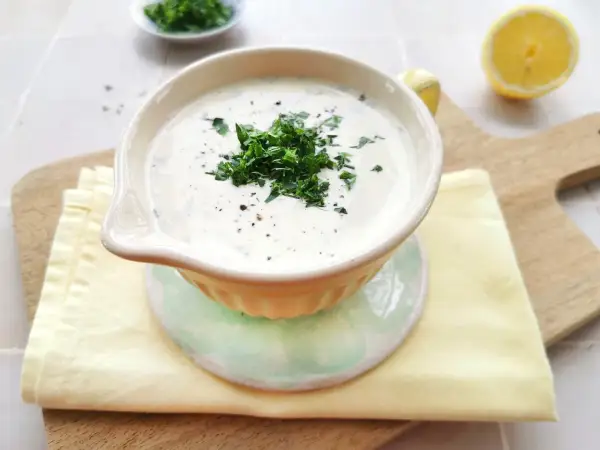Cremige Schüssel mit frischem Ranch Dressing, garniert mit Petersilie und Pfeffer. Daneben liegen Zitronenspalten und ein Stapel Servietten.