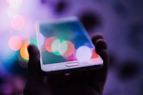 Dłoń trzyma telefon z kolorowymi światłami na ekranie. Chcesz wiedzieć, jak zrobić zdjęcie z filmu na telefonie?