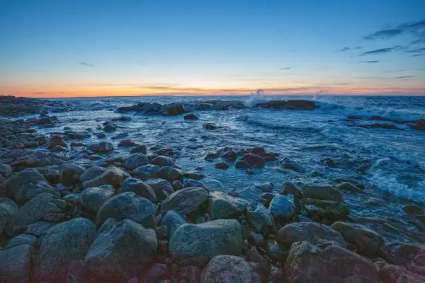 Stenstrand vid solnedgången. Vågor slår mot klipporna i det blåa vattnet. En lugn kväll, precis som det iso betyder.