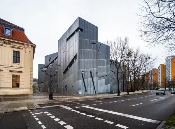Nowoczesny budynek muzeum żydowskiego w Berlinie, obok starszej kamienicy, z charakterystyczną, poszarpaną fasadą.