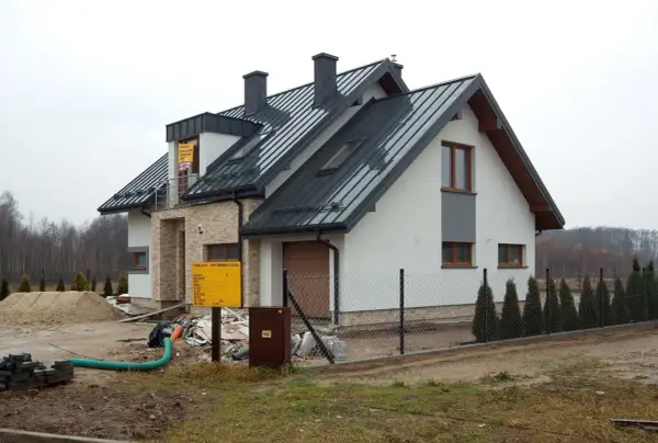 Nowy dom w budowie, widoczny przyłącze napowietrzne, plac budowy z piaskiem i materiałami.
