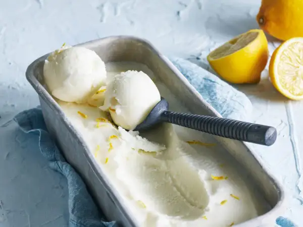 En metallform fylld med krämig italiensk citronsorbet, garnerad med citronskal. Två skopor är upptagna med en skopa.