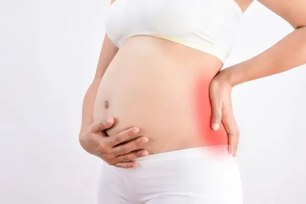 Femme enceinte tenant son ventre, une zone rouge sur le côté indique une douleur au fessier en fin de grossesse.