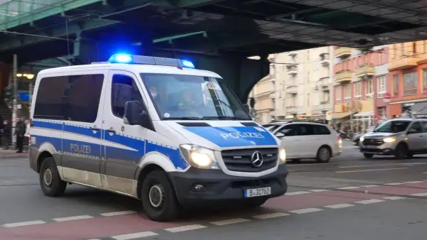 Polizeivan mit Blaulicht fährt auf der Straße. Ein polizeiliches Verkehrszeichen ist auf dem Fahrzeug angebracht.