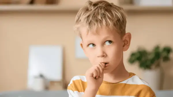 Chłopiec z blond włosami obgryza paznokcie, zastanawiając się, dlaczego dzieci to robią.