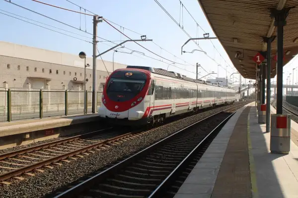 Nowoczesny pociąg Renfe z czerwonym przodem stoi na stacji. W tle budynek i peron.