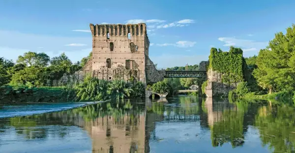 Rovine di un castello e un ponte sul Mincio, con riflessi sull'acqua calma.