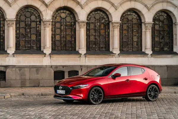 Un elegante Mazda 3 Skyactiv X rojo, con sus líneas fluidas, se detiene frente a una fachada histórica con arcos y vidrieras.